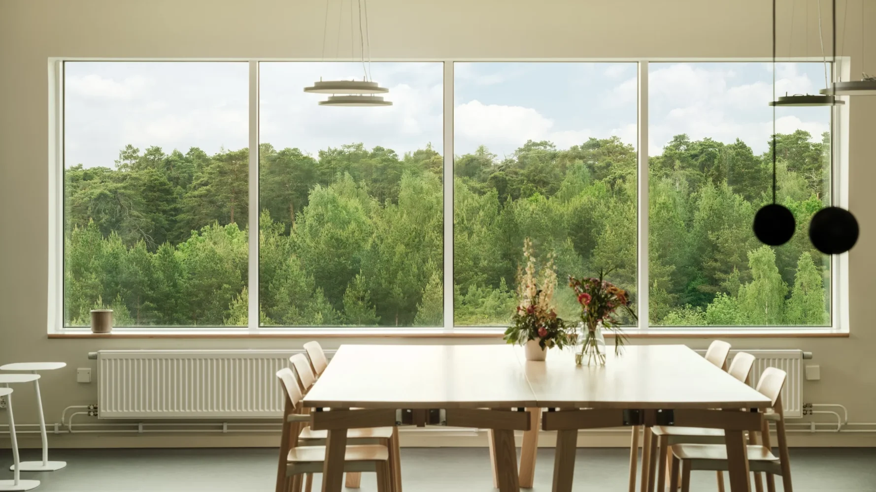 Interior image of a bright lunchroom with large windows, plants and modern furniture.