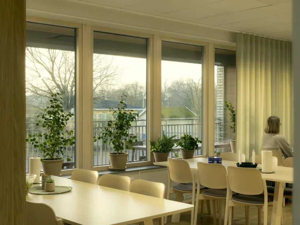 Interior image of a bright lunchroom with large windows, wood panels, plants and modern furniture.