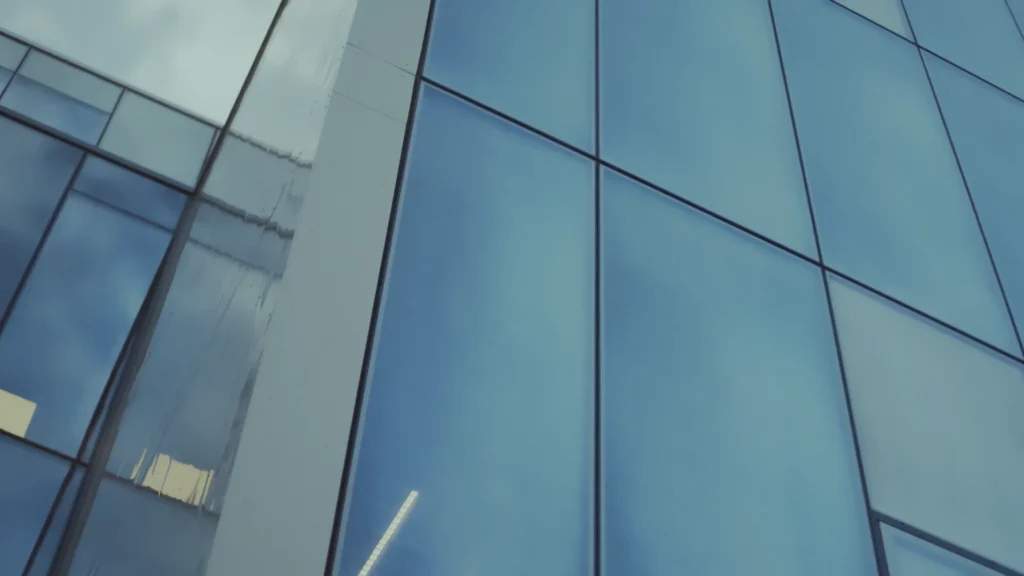 Reflective glass facade against a blue sky with a cloud reflected in the surface.