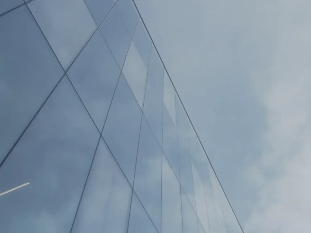 Reflective glass facade against a blue sky with a cloud reflected in the surface.