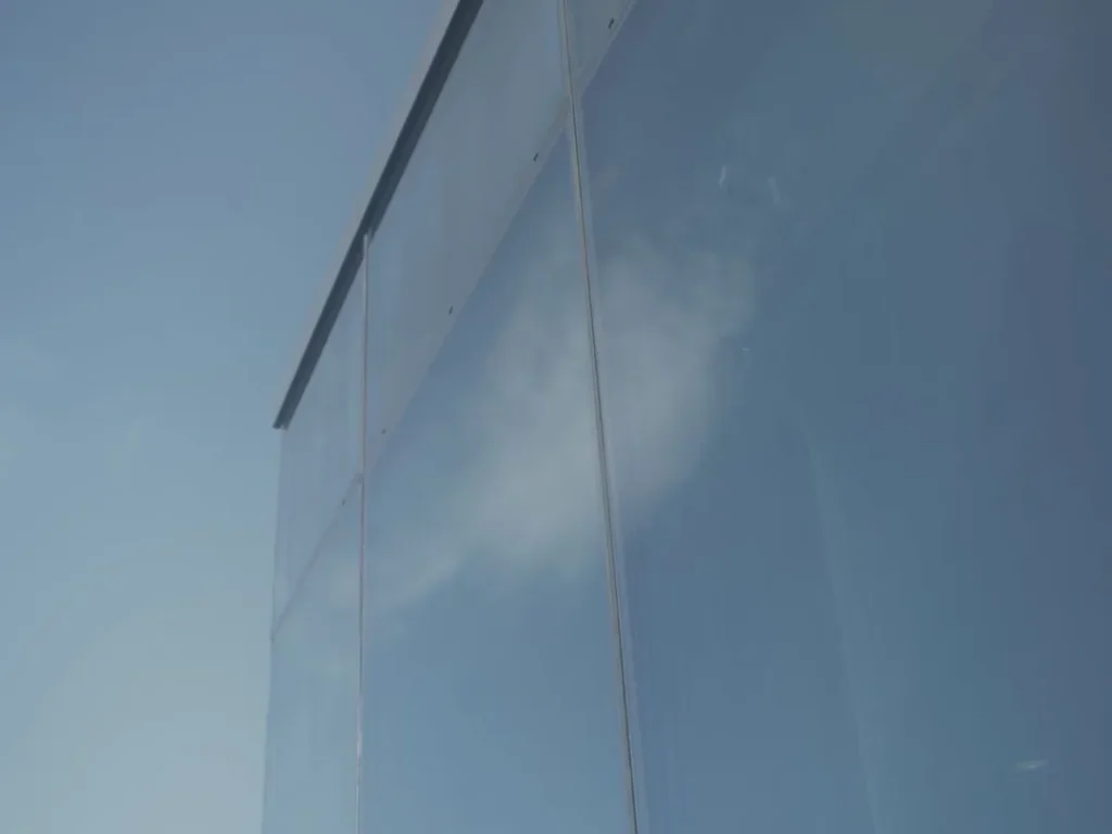 Reflective glass facade against a blue sky with a cloud reflected in the surface.