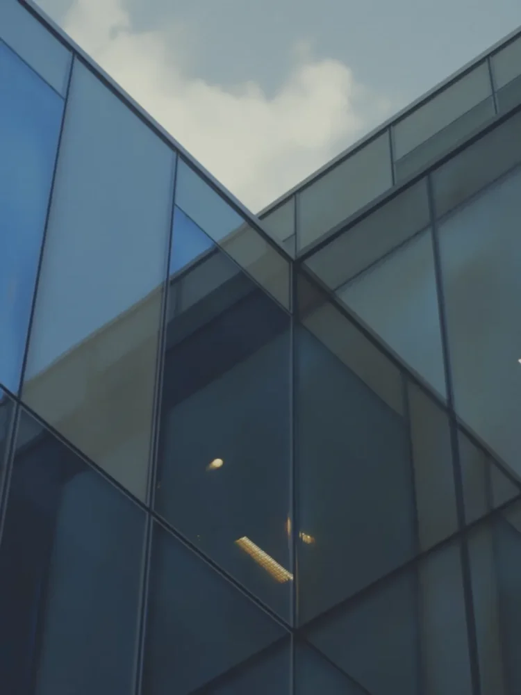 Reflective glass facade against a blue sky with a cloud reflected in the surface.
