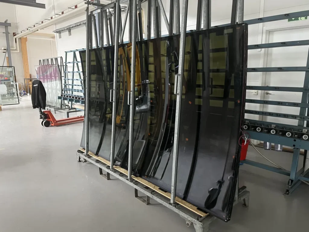 Two large curved glass panes lie on a metal table with suction cups, in a workshop environment.