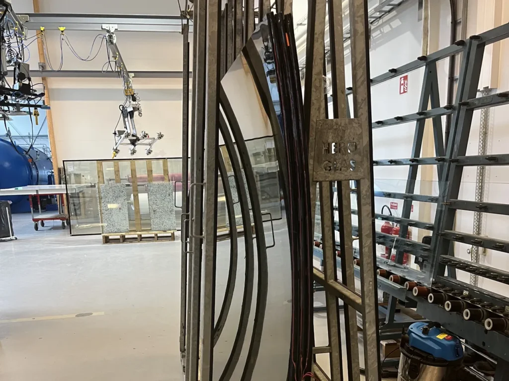 Two large curved glass panes lie on a metal table with suction cups, in a workshop environment.