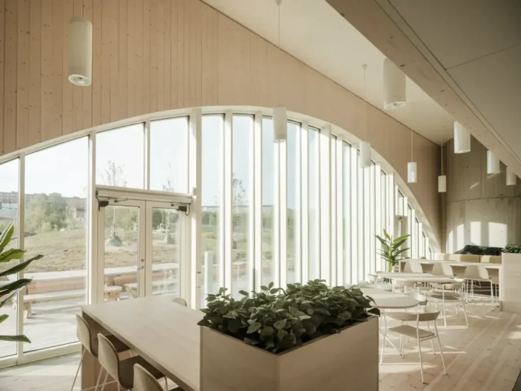 Interior image of a bright lunchroom with large windows, wood panels, plants and modern furniture.