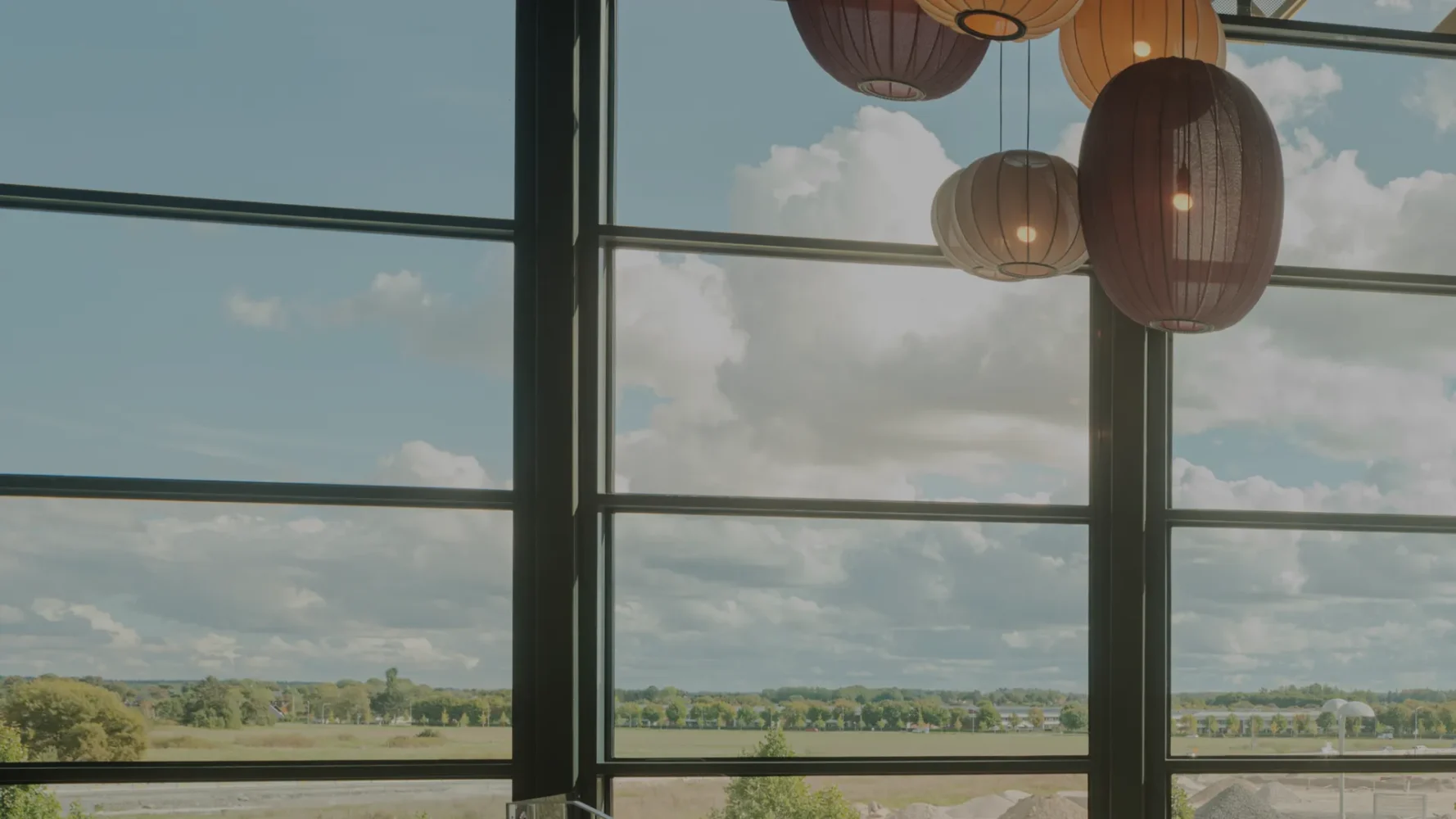 Large windows overlooking landscape and cloudy sky, decorated with decorative lamps.