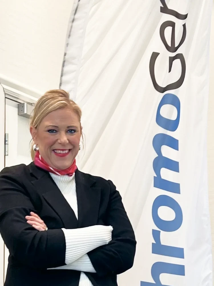 Portrait of woman in business attire standing in front of a white flag with the text "ChromoGenics".
