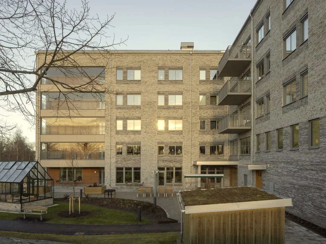 Light brick apartment building with several floors and windows in a regular rhytm, photographed in morning light.