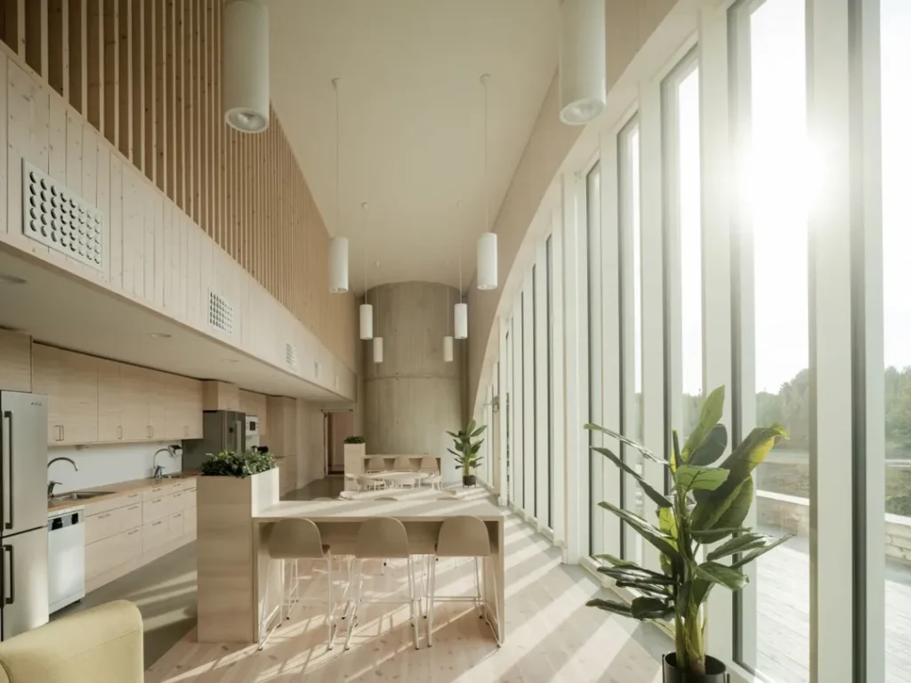 Interior image of a bright lunchroom with large windows, wood panels, plants and modern furniture.