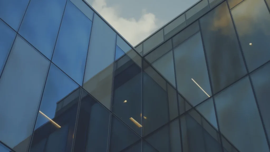 Reflective glass facade against a blue sky with a cloud reflected in the surface.