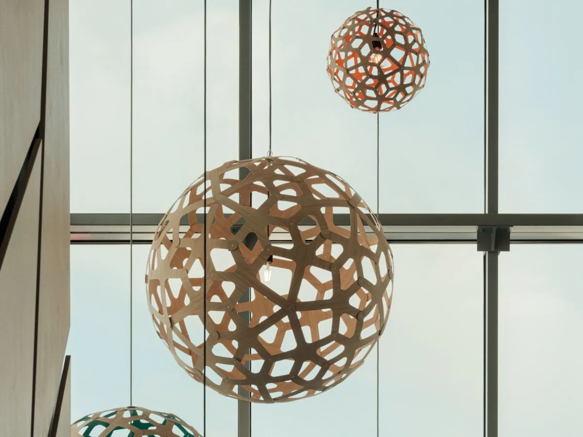 Nahaufnahme von hängenden, kugelförmigen Lampen in Holzoptik, im Hintergrund ist ein großes Fenster zu sehen.