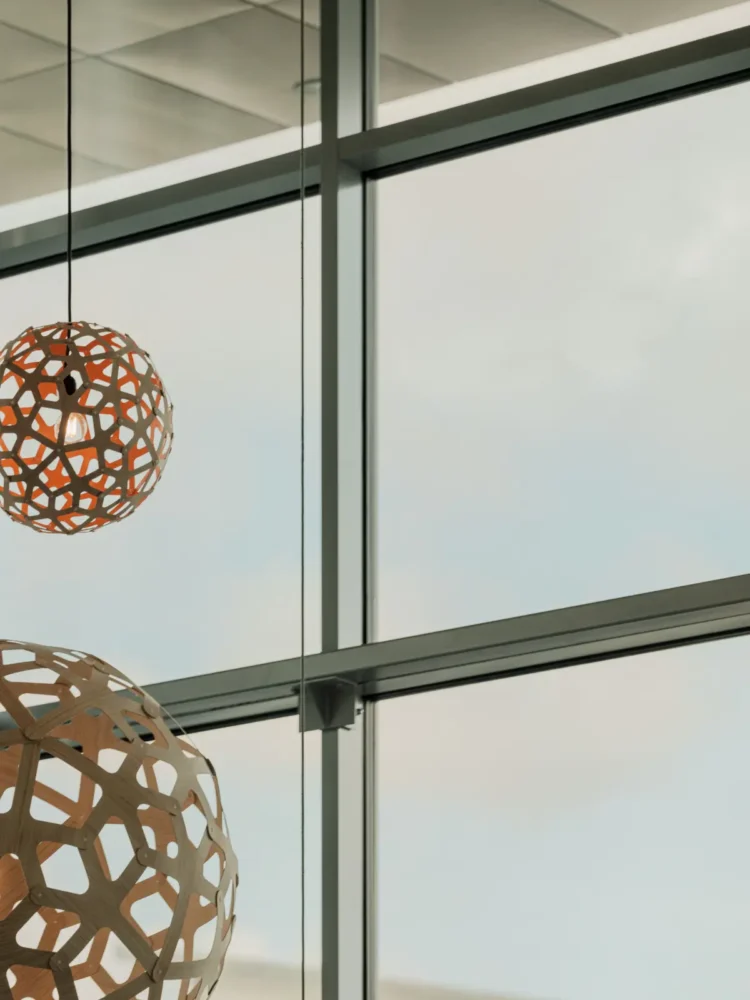 Close-up of hanging, spherical lamps in wood-like pattern, with a large window in the background.