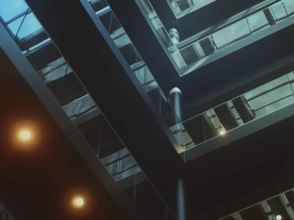 View upwards in a modern multi-storey office building, with glass windows and visible lights.