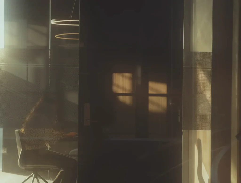 Woman sitting in meeting room behind glass wall, with sunlight creating shadows in the room.