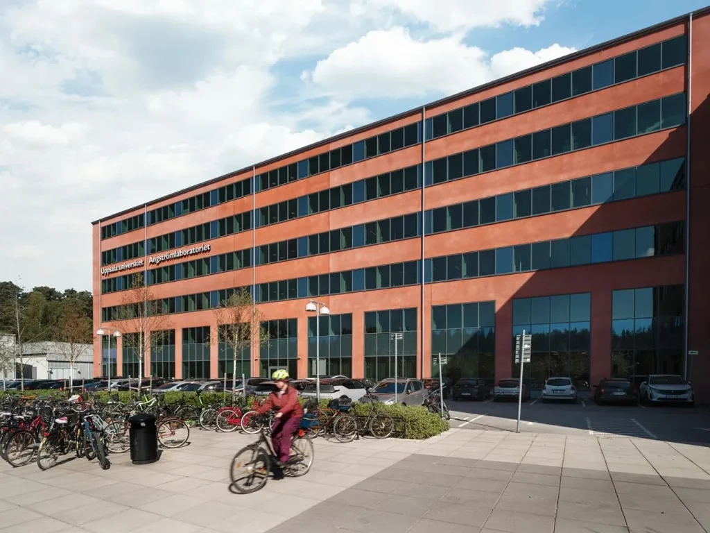 Red building with large glass sections and the text 'Uppsala University Ångström Laboratory' on the facade.