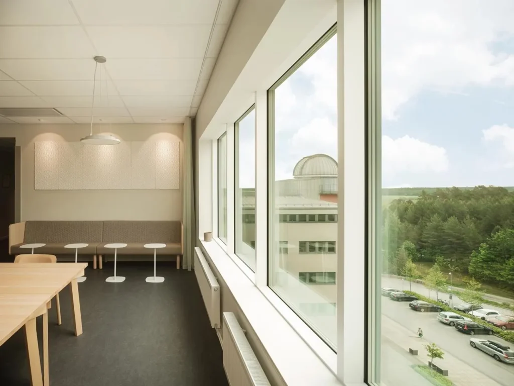 Interior image of a bright lunchroom with large windows, plants and modern furniture.
