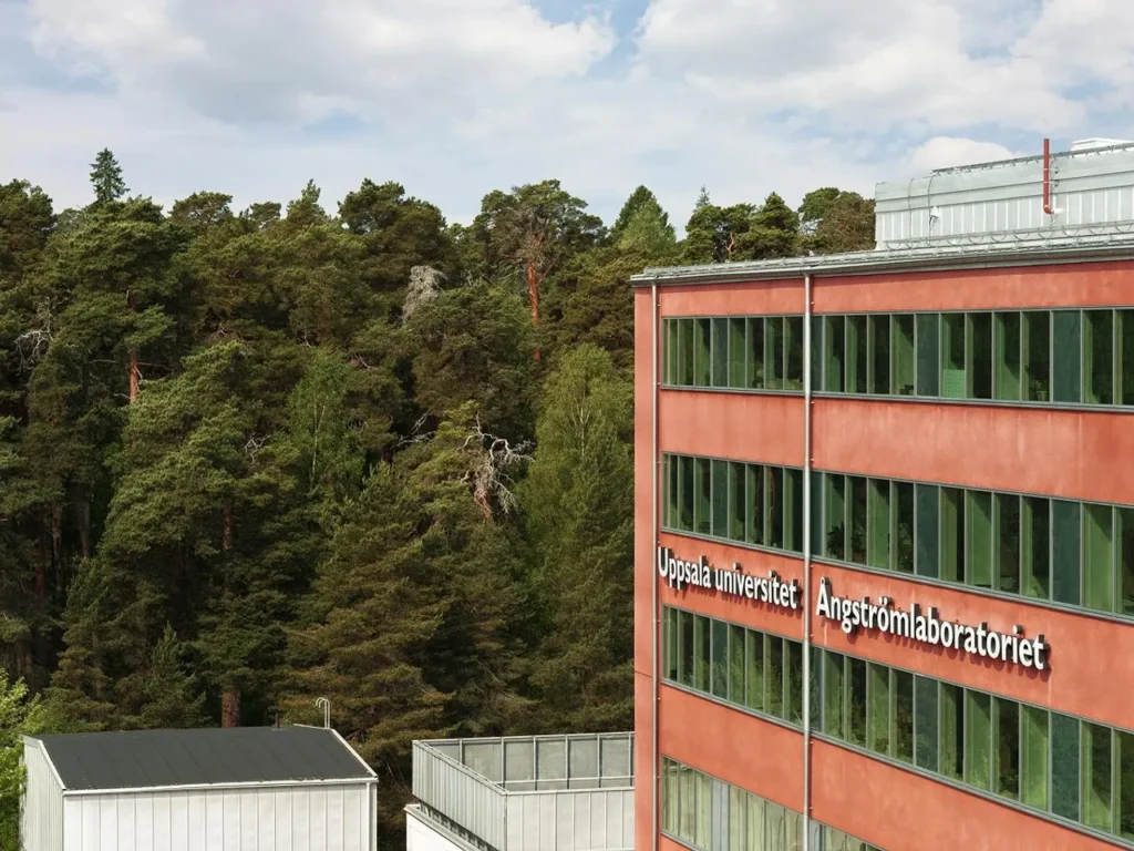 Red building with large glass sections and the text 'Uppsala University Ångström Laboratory' on the facade.