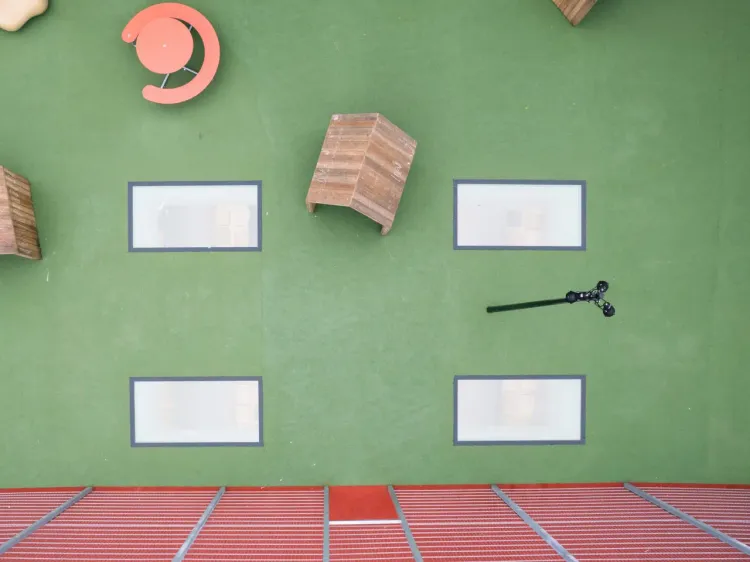 Bird's eye view of a green courtyard with windows in the floor and play equipment on top.