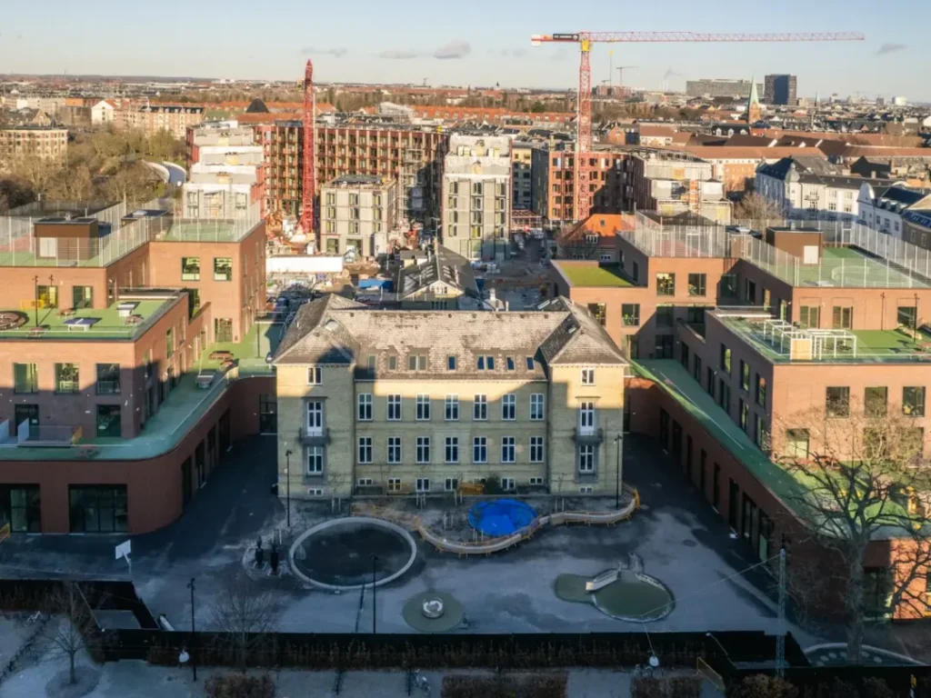 Fågelvy över en skola eller bostadsområde i stadsmiljö, med byggarbetsplats i bakgrunden.