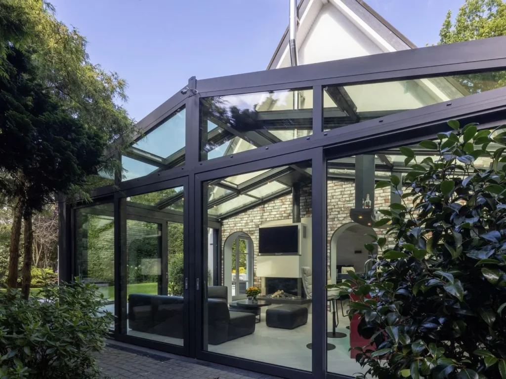 Glass pavilion in a garden setting with a black frame and open glass sections that let in daylight.