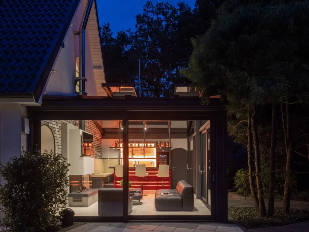 Glass pavilion in a garden setting with a black frame and open glass sections that let in daylight.