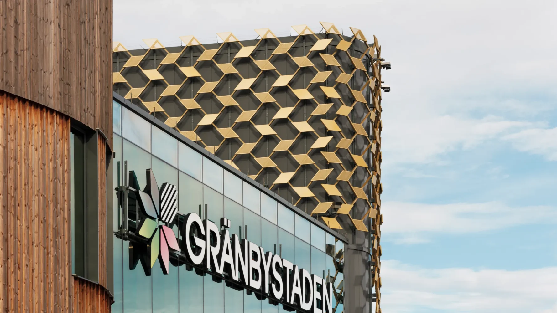 Exterior of Gränbystaden shopping center with gold-colored facade decoration in a geometric pattern and reflective glass.