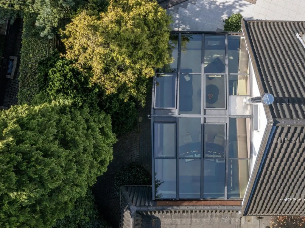 Aerial view of a glass roof of a house surrounded by greenery and brick walls.