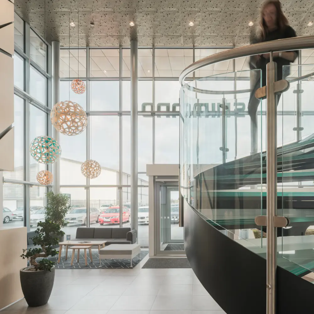 Entrance to an office building with glass walls, a spiral staircase in metal and glass, and decorative lights.