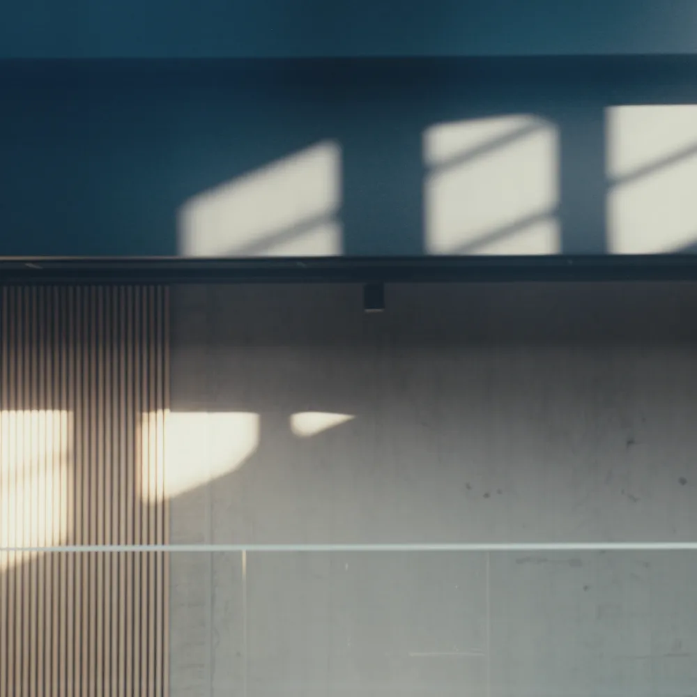 Sunlit wall with vertical wooden panels and glass railing, where window shadows are projected at different angles.